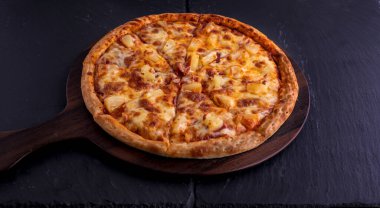 Hawaii pizzası kesme tahtasında izole edilmiş koyu arka planda İtalyan fast food 'u.