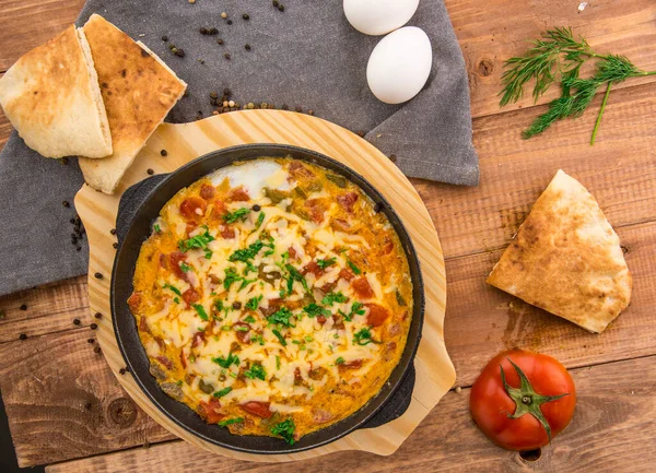 Tomato frying pan with eggs and cheese served in dish isolated on table side view of arabic food
