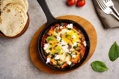 Geleneksel Shakshuka, yumurtalı, domatesli ve ekmekli kızartma tavasında servis edilen Arap kahvaltısı masasının üstünde izole edilmiş.