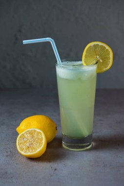 Sağlıklı limon suyu, limon dilimi ve gri arka planda saman manzaralı bardakta servis edilen taze meyve suyu.
