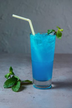 Sağlıklı Mavi Göl Mojito sodası. Gri arka planda saman kenar görüşlü cam servis ediliyor.