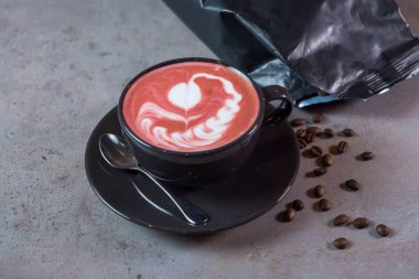 Kahve fincanında servis edilen sıcak pancar Latte sanatı ve gri arka planda kaşık ve fasulye yan görünümü.