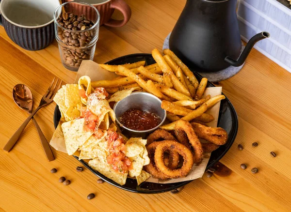 Snacks platter with french fries, fried onion rings, nachos, chilli sauce, coffee beans, fork, spoon served in dish isolated on wooden table top view of taiwan food