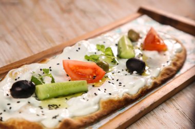 Zeytinli, domatesli ve salatalıklı Labneh pizza arkaplanda izole edilmiş ahşap tahtada servis edilir.