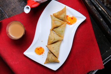 Samosa, sambosa, sos, çay ve çaydanlıkla servis edilen kırmızı hasırla servis edilen masa Arap yemeklerinin üst görüntüsü.