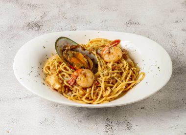 Karides ve karidesli deniz ürünleri aglio spagettisi izole edilmiş gri arka planda servis edilir.