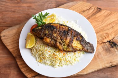 Beyaz pirinçli Shiri Fish kızartması, domates ve limonlu, ahşap masa manzaralı, orta doğu yemeği.