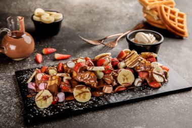Muz, çilek, çikolatalı marshmallow Waffle. Masanın üstünde gözleme, waffle ve tatlı var.