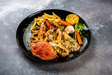 Karides, karides, yengeç, patates kızartması, salata ve limonla karıştırılmış deniz mahsulü ızgara. Arka plandaki Arap yemeklerinin üst görüntüsünde servis ediliyor.