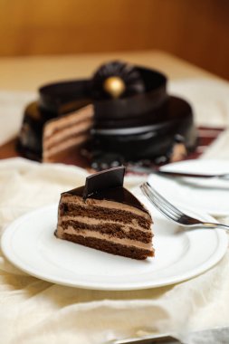 Black Forest Pastası dilimleri arasında çikolata parçacıkları, çatal, sofra kenarında izole edilmiş tabakta servis edilen şeker, fırın kafesi yer alıyor.