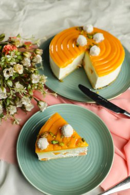 Mango Yoğurtlu kek dilimi. Üstünde şam fıstığı çatalı ve tabakta servis edilen çiçekler. Peçete tarafında izole edilmiş kafe manzaralı yemekler.