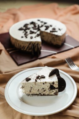 Oreo Cheesecake dilimleri arasında çikolata, krema, çatal ve çiçeklerle servis edilen ve peçete tarafından izole edilmiş tabakta servis edilen şeker ve kafe yemekleri yer alıyor.