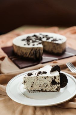 Oreo Cheesecake dilimleri arasında çikolata, krema, çatal ve çiçeklerle servis edilen ve peçete tarafından izole edilmiş tabakta servis edilen şeker ve kafe yemekleri yer alıyor.