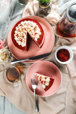 Kaliteli kırmızı kadife kek ve dilimler arasında krema, çatallı şeker, bir fincan kahve ve kahve var.