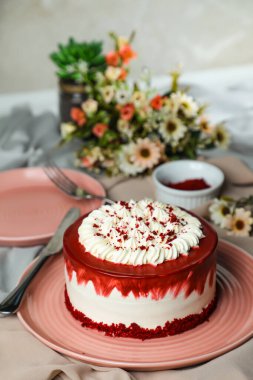 Kırmızı kadife kek, krema, çatallı şeker, bıçak ve çiçeklerle servis edilen tabakta servis edilen ve peçete tarafından izole edilmiş kafe yemekleri içerir.