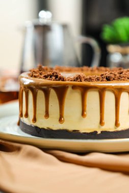 Tuzlu Karamelli Sarışın kek, çikolatalı krema, çatallı şeker, bir fincan kahve ve kafeterya manzaralı peçete tarafında servis edilen çömlek