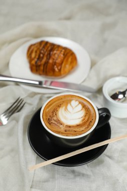 Sıcak Macchiato Kahve Latte Art kruvasan, poğaça, ekmek ve bıçakla servis edilir. Peçete manzaralı kafe kahvaltısına izole edilmiş.