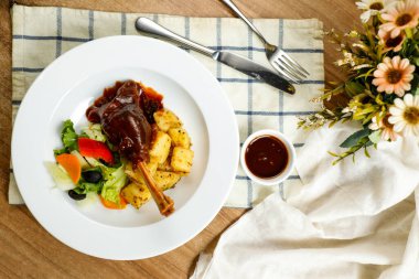 Kuzu Ossobuco ya da Osso buco kuzu budu patates, sos, bıçak, çatal ve salata ile servis edilen tabakta servis edilen peçete manzaralı et yemeği