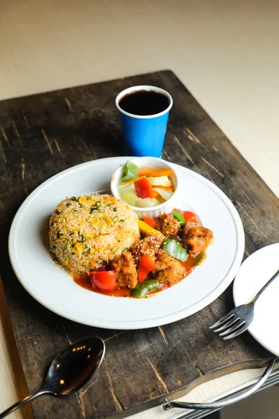 Chili Chicken Rice Meal served in plate with sauce, cold drink, spoon and fork isolated on wooden board side view of thai food