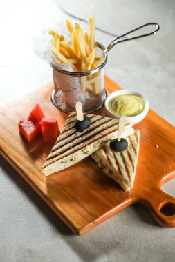 Izgara tavuklu sandviç ve patates kızartması kovası. Tahtada servis ediliyor. Kahvaltı masasının peçete tarafından izole edilmiş.