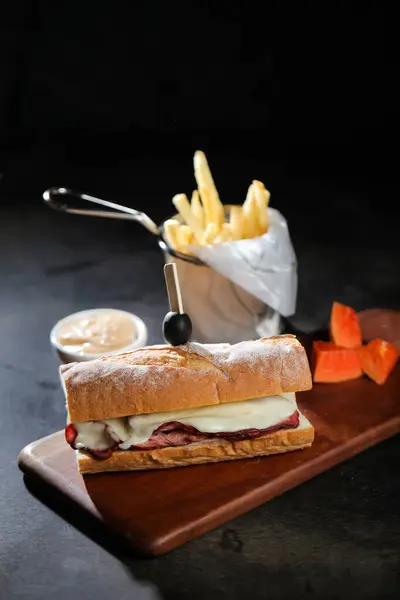Roasted Beef Sub Sandwich with french fries bucket served on wooden board isolated on dark background side view of breakfast foodRoasted Beef Sub Sandwich with french fries bucket served on wooden board isolated on dark background side view of breakf