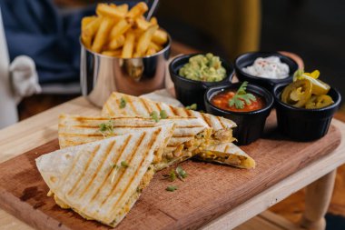 Tavuk Quesadillas taco dürümü, acılı sos ve patates kızartması kovası. Tahta tahtada servis ediliyor.