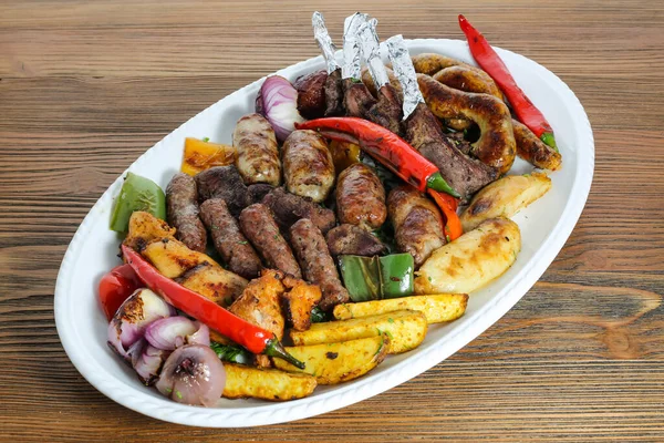 Mix grill family platter tikka kabab, lamb chop, meat kebab, chicken, beef, mutton, potato veggies, tomato and onion served in dish isolated on table side view of arabic food