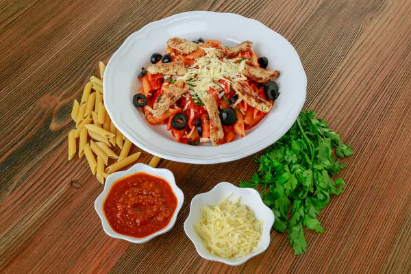 Grilled chicken pasta with black olive, chili sauce and coriander served in dish isolated on table side view of arabic food
