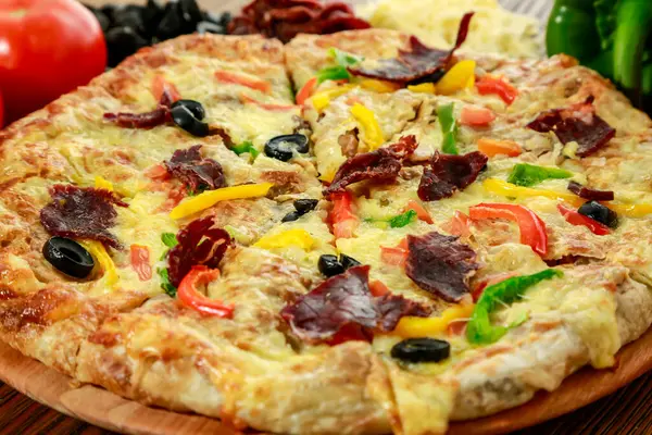 Pastrami and eggs pizza pie with bell pepper, tomato and black olive served in wooden board isolated on table side view of arabic food
