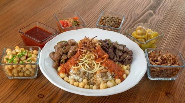 Koushari egyptian food with chicken liver and beef kebab, chickpea, noodles, boiled rice, lentil, fried onion, tomato, chili sauce and pickle served in dish isolated on table top view of arabic food