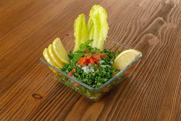 Tabbouleh salad with cucumber, tomato, onion, mint and lemon slice served in dish isolated on wooden table side view of arabic food