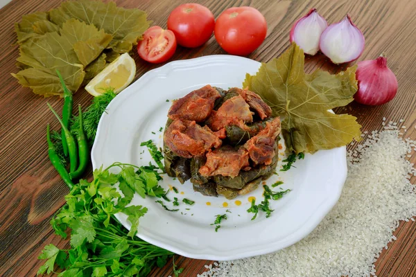 vine leaves meat casserole with tomato, onion, rice, coriander, lemon slice and green chilli served in dish isolated on wooden table side view of arabic food