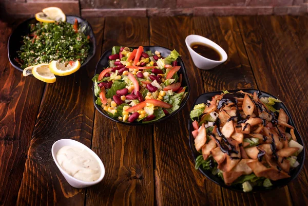 Assorted salads with tomato, cucumber, onion, cabbage, lettuce leaves, lemon slice, spinach and red beans served in dish isolated on wooden table side view of arabic food