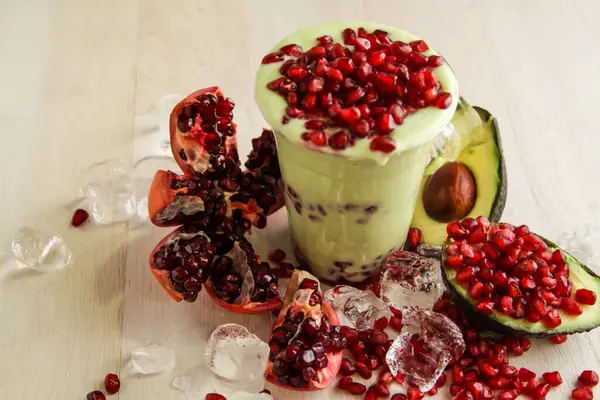 Avocado smoothie with pomegranate seeds served in disposable glass isolated on table side view of healthy drink