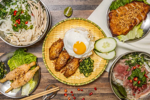 Chicken Wings with Fried Egg sunny side up and Rice, Vietnamese Sugar Cane with Shrimps, Grilled Pork Jowl steak, Hanoi rare Beef Pho and Shredded Chicken and Sausage Pho served in dish isolated on wooden table top view of hong kong fast food