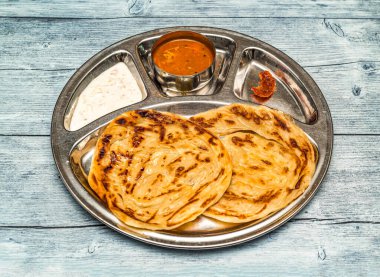 Roti prata, paratha, parata, köri, raita ve turşulu poratha ahşap masa üzerinde Hint baharatlı yemeklerinin üst görüntüsünde servis edilir.