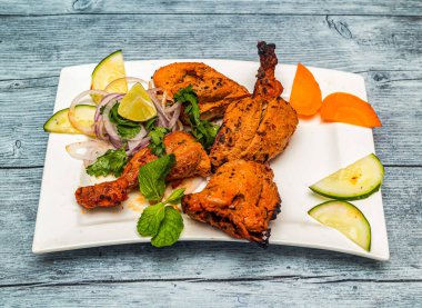 Limonlu ve soğanlı ızgara tandır tavuğu ahşap masa üstünde Hint baharatlı yemeklerinin üstünde servis edilir.