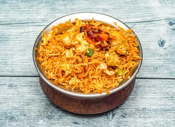 mixed non veg fried rice or chicken and shrimp biryani served in copper dish isolated on wooden table top view of indian spicy food