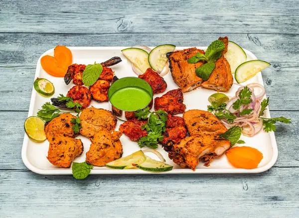 tandoori platter with tandoori chicken , tikka kabab, and grilled prawn with onion and lemon served in dish isolated on wooden table top view of indian spicy food