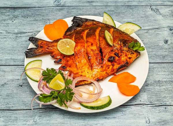tandoori pomfret fish fry with lemon and onion served in dish isolated on wooden table top view of indian spicy food