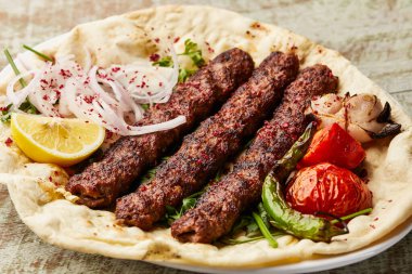 Arap Et Kebabı safran, soğan, domates, pita ekmeği, limon dilimi ve salata ile servis edilir.
