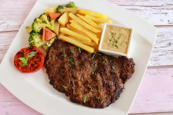 BEEF STEAK with french fries, mayo dip, tomato, broccoli and cucumber salad served in dish isolated on table closeup top view of fastfood spices food