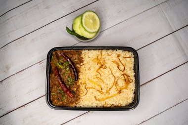 Achari bifteği pulao biryani pilavı, salatalık ve limon dilimi ile servis edilir. Tahta masa üzerinde, bangladeş ve Hint baharatlı yiyeceklerinin üst görüntüsünde.