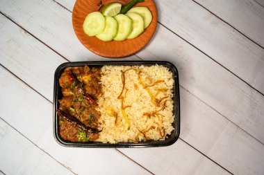 Achari tavuklu pulao biryani pilavı, salatalık ve limon dilimli, ahşap masa üstünde, bangladeş ve Hint baharatlı yemeklerinin yakın planında servis edilir.