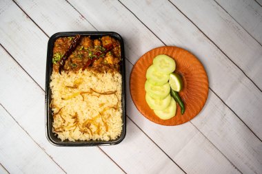 Achari tavuklu pulao biryani pilavı, salatalık ve limon dilimli, ahşap masada servis edilmiş. Bangladeş ve Hint baharatlı öğle yemeği manzaralı.