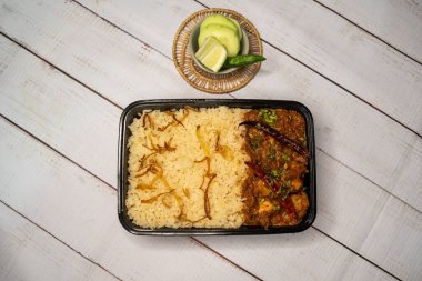 Achari tavuklu pulao biryani pilavı, salatalık ve limon dilimli, ahşap masa üzerinde, bangladeş ve Hint baharatları sokak yemeklerinin üst görüntüsünde servis ediliyor.