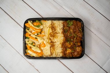 Tavuk Bhuna pulao biryani pilavı, salatalık, sos ve limon dilimi ile birlikte ahşap masa üzerinde, bangladeş ve Hint baharatlı öğle yemeği manzarasında servis edilir.