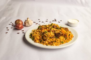 Mughlai Biftek Biryani pilavı sarımsak, soğan ve raita ile servis edilmiş arka planda Hint ve Pakistanlı geleneksel yemeklerin arka planında izole edilmiş.
