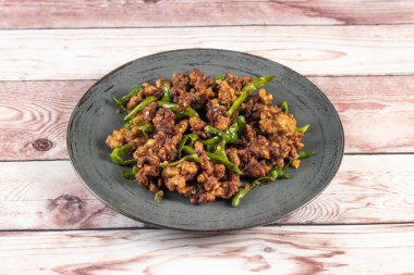 Kızarmış yeşil biberli tavuk. Tabakta servis ediliyor. Tahta masa kenarında bangladeş yemeği.