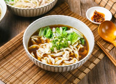 Acı biber soslu etli şehriye çorbası, taze soğan, ahşap kaşık ve yemek çubukları Tayvan yemeğinin yanında servis edilir.